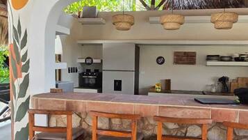 An outdoor bar area with a thatched roof, stone counter, and wooden stools.