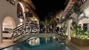 Ein Schwimmbecken mit einer Holzbrücke, umgeben von weißen Mauern und Palmen.