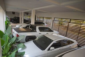 Un parking à étages où de nombreuses voitures sont garées en rangées, de grandes fenêtres équipées de stores et une plante au premier plan.
