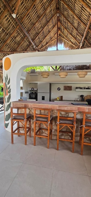 An outdoor bar area with a thatched roof, stone counter, and wooden stools. - Selanna 6 Gibosa Menguante Acogedora y Cálida (El Paredon)