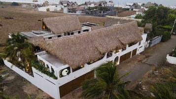 A building with thatched roofs and a white exterior, surrounded by palm trees and a coastal view.