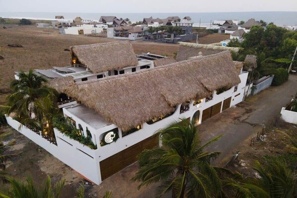 A building with thatched roofs and a white exterior, surrounded by palm trees and a coastal view. - Selanna 6 Gibosa Menguante Acogedora y Cálida (El Paredon)