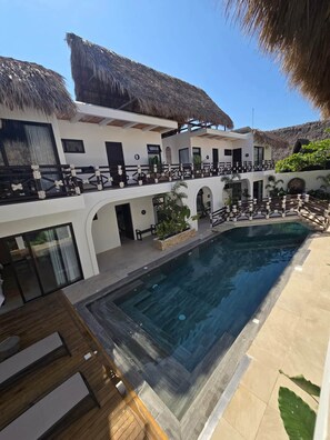 Un resort con piscina, construcciones de techo de paja y un edificio de varios niveles.