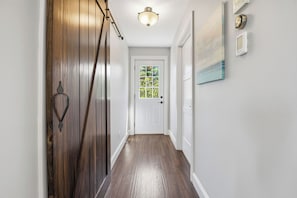 A hallway with a wooden door, a white door with a window, and a light fixture on the ceiling. - Modern 2BR Oceanfront Cottage with Fireplace & Beach Access (Malagash)