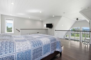 A bedroom with a large bed, a television mounted on the wall, and a balcony with a view. - Modern 2BR Oceanfront Cottage with Fireplace & Beach Access (Malagash)