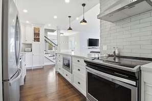 A modern kitchen with white cabinetry, stainless steel appliances, and a wooden floor. - Modern 2BR Oceanfront Cottage with Fireplace & Beach Access (Malagash)