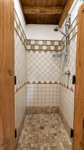 A shower with a tiled floor and walls, a wooden ceiling, and a showerhead.