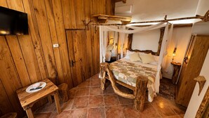 Um quarto rústico de madeira com uma cama, uma mesa pequena e uma TV fixada na parede.