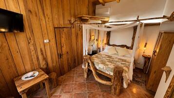 Une pièce rustique en bois, avec un lit, une petite table et un téléviseur fixé au mur.