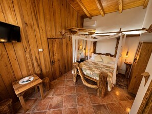 Een eenvoudige houten kamer met een bed, een kleintje tafeltje en een aan de muur bevestigde televisie.