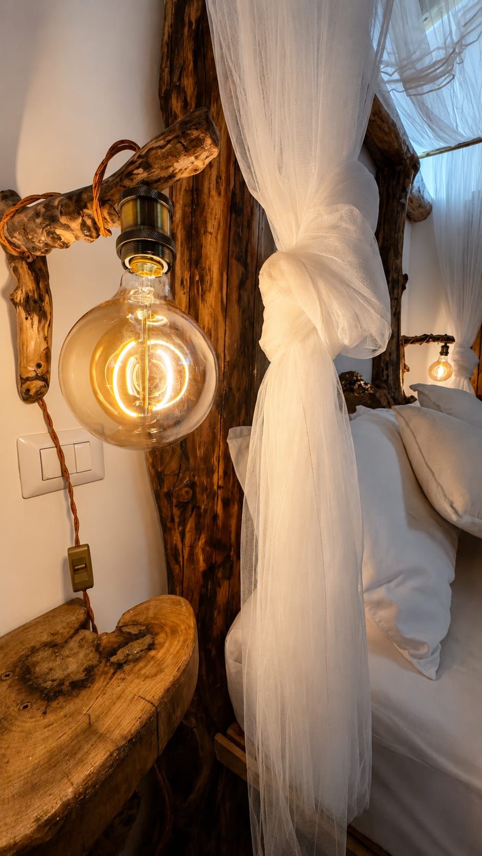 Une pièce avec un lit, un luminaire suspendu et une chaise en bois.