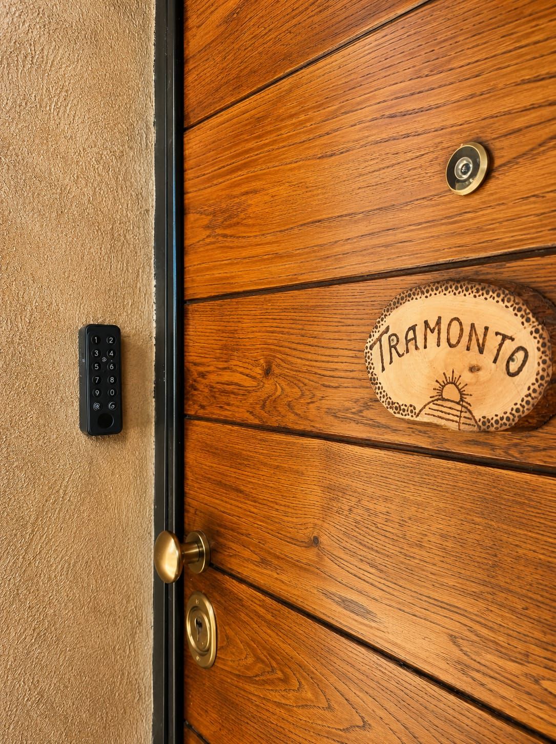 Eine Holztür mit Messingklinke und Schlüsselloch, einer Tastaturverriegelung und einer Namensschild mit der eingravierten Aufschrift 'TRAMONTO'.