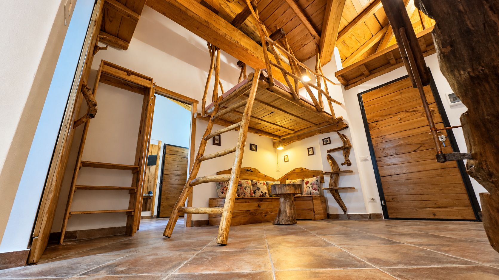 Ein rustikaler Innenraum mit einer Holzleiter, einem Bett mit floralen Kissen und einer großen Holztür.