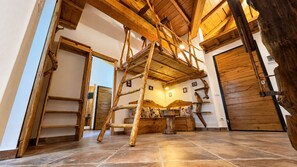 A rustic interior with a wooden ladder, a bed with floral pillows, and a large wooden door.