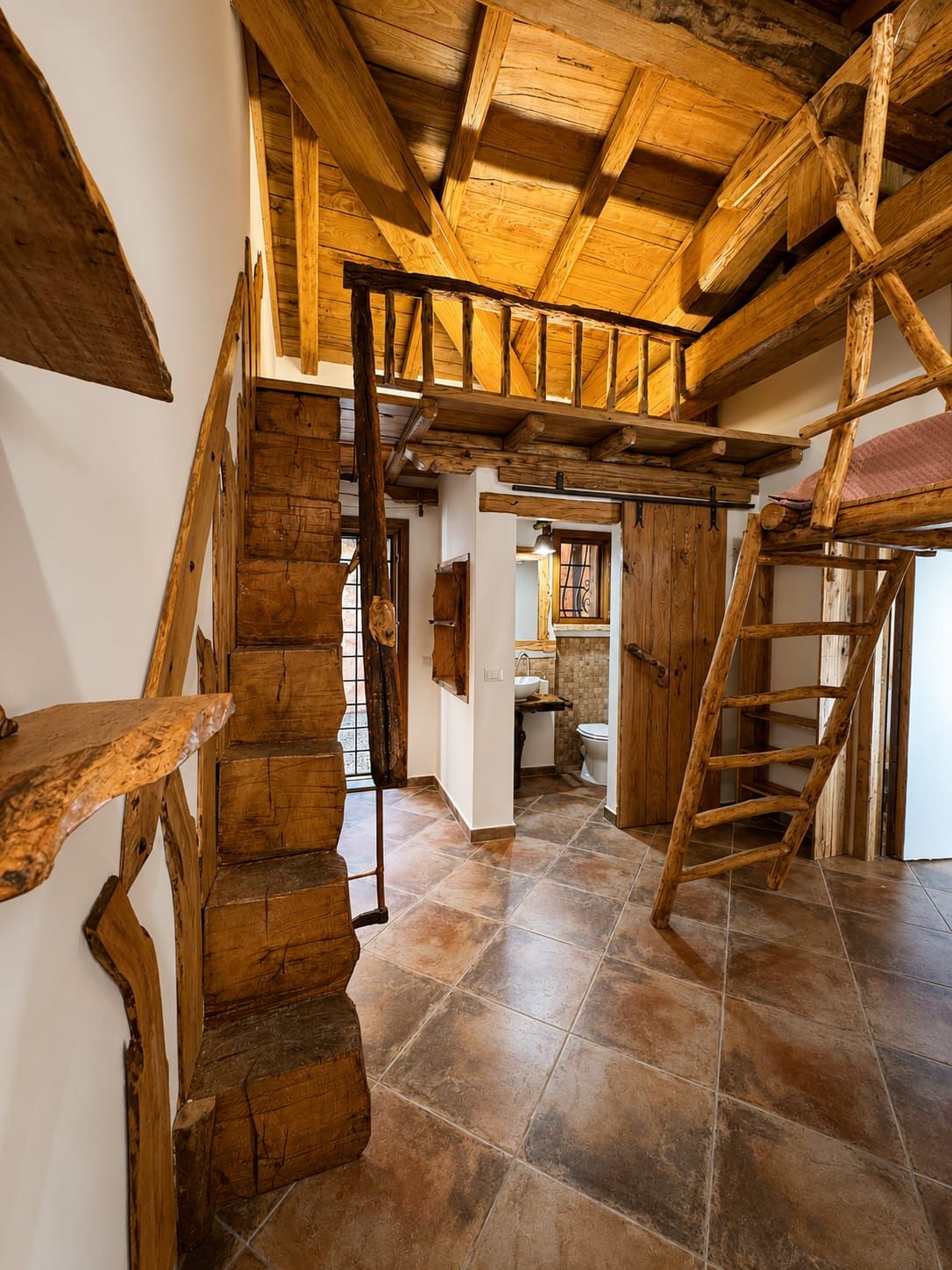 Un interior rústico con una escalera de madera, techo de madera y un baño con lavamanos e inodoro.