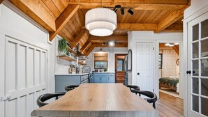 Una cocina moderna con una mesa y sillas de madera, una lámpara colgante y vistas a un dormitorio.