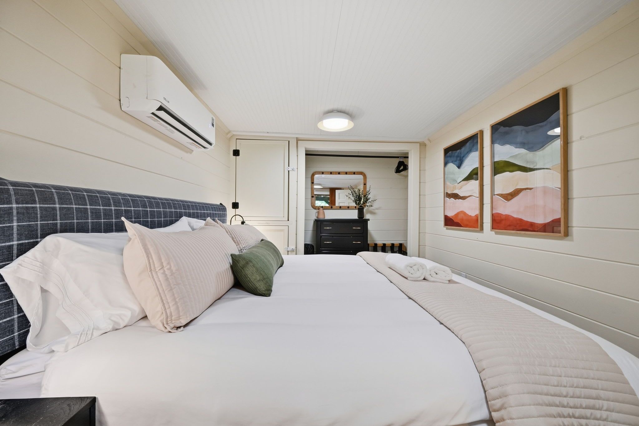A hotel room with a bed, a dresser, a mirror, and two paintings on the wall.
