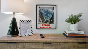 Un cartel enmarco de Carolina del Norte, una lámpara, un conjunto de reglas para el jacuzzi enmarco, un control remoto y una planta sobre una superficie de madera.