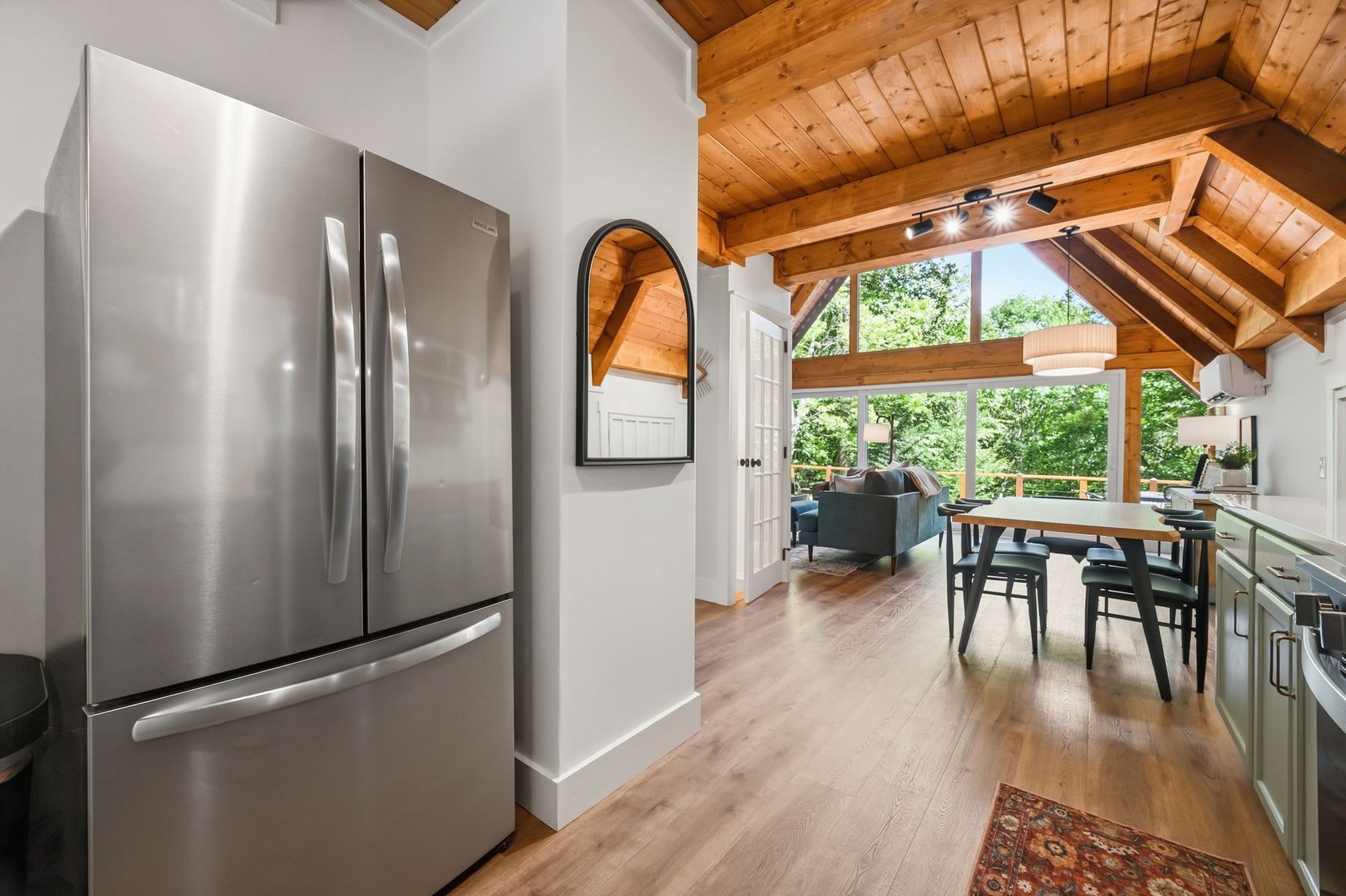 A modern kitchen with a stainless steel refrigerator, wooden ceiling beams, and a dining area with a table and chairs.
