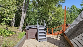 A wooden deck with a metal staircase leading to a covered area, surrounded by trees and gravel.
