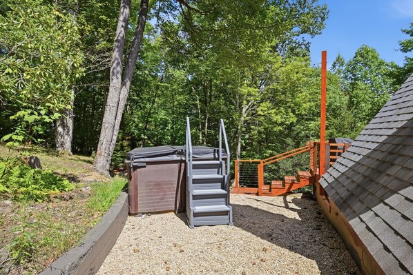A wooden deck with a metal staircase leading to a covered area, surrounded by trees and gravel.