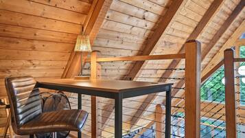 A wooden interior with a table and chair, a lamp, and a view through a window.