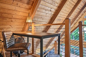A wooden interior with a table and chair, a lamp, and a view through a window.
