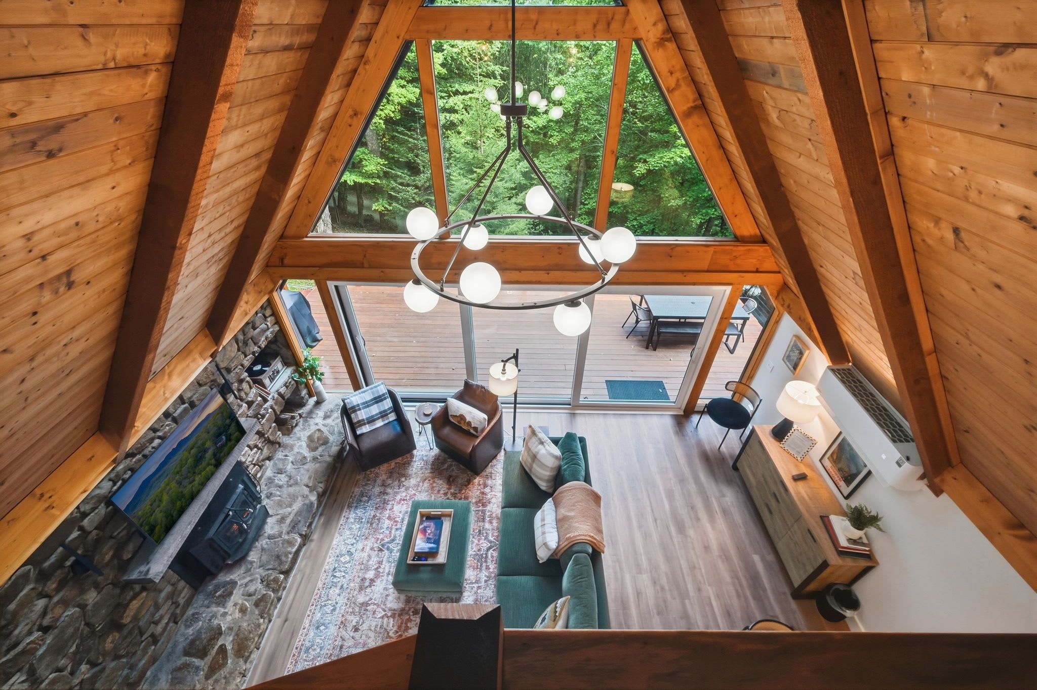 A high-ceilinged wooden interior with a stone fireplace, a sofa, and a dining area with outdoor views.