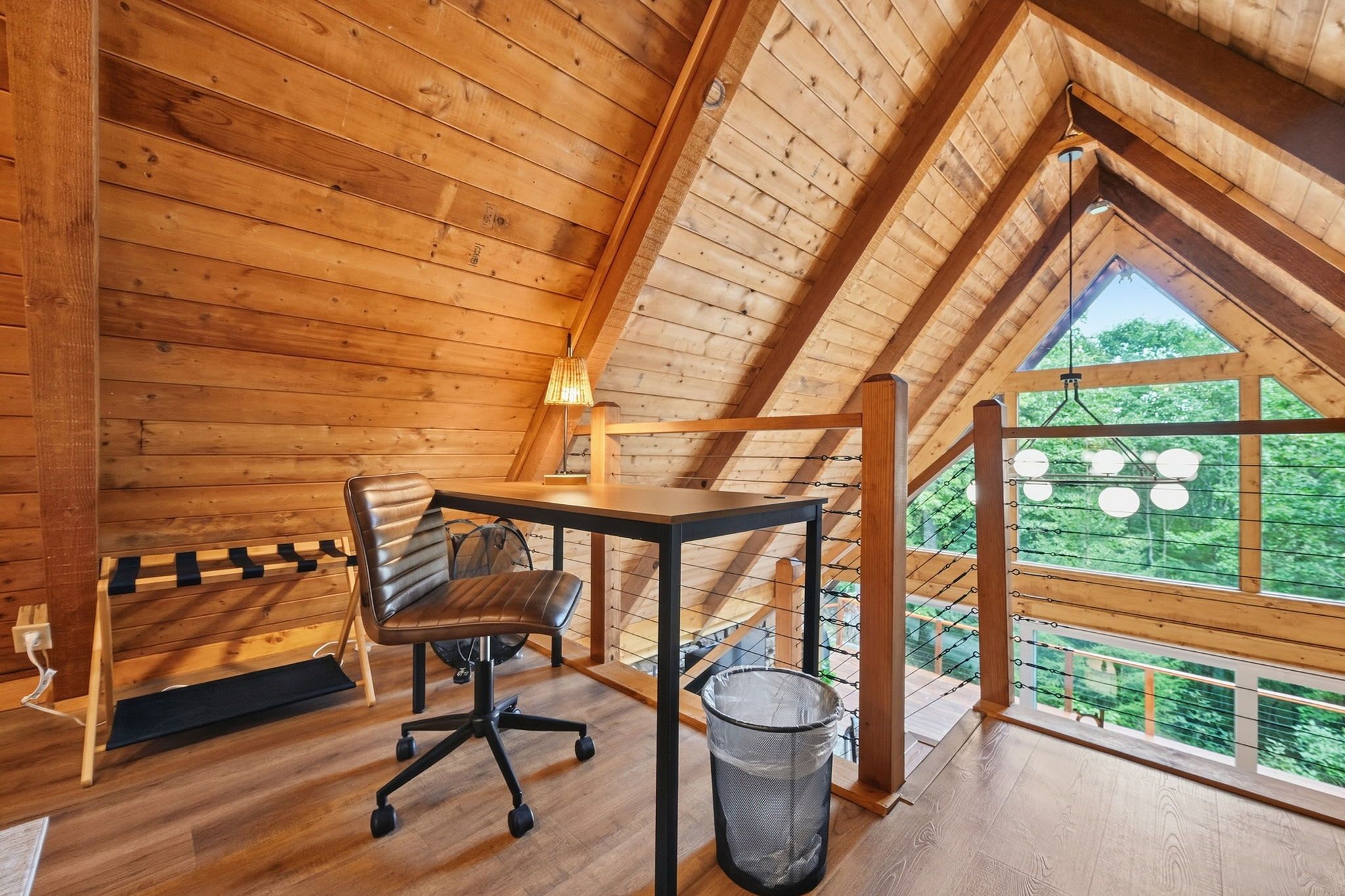 A wooden interior with a desk, chair, and a view of greenery outside.