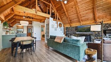 A spacious living area with a high ceiling, a fireplace, and a dining area with a table and chairs.