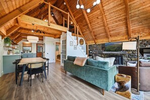 A spacious living area with a high ceiling, a fireplace, and a dining area with a table and chairs.