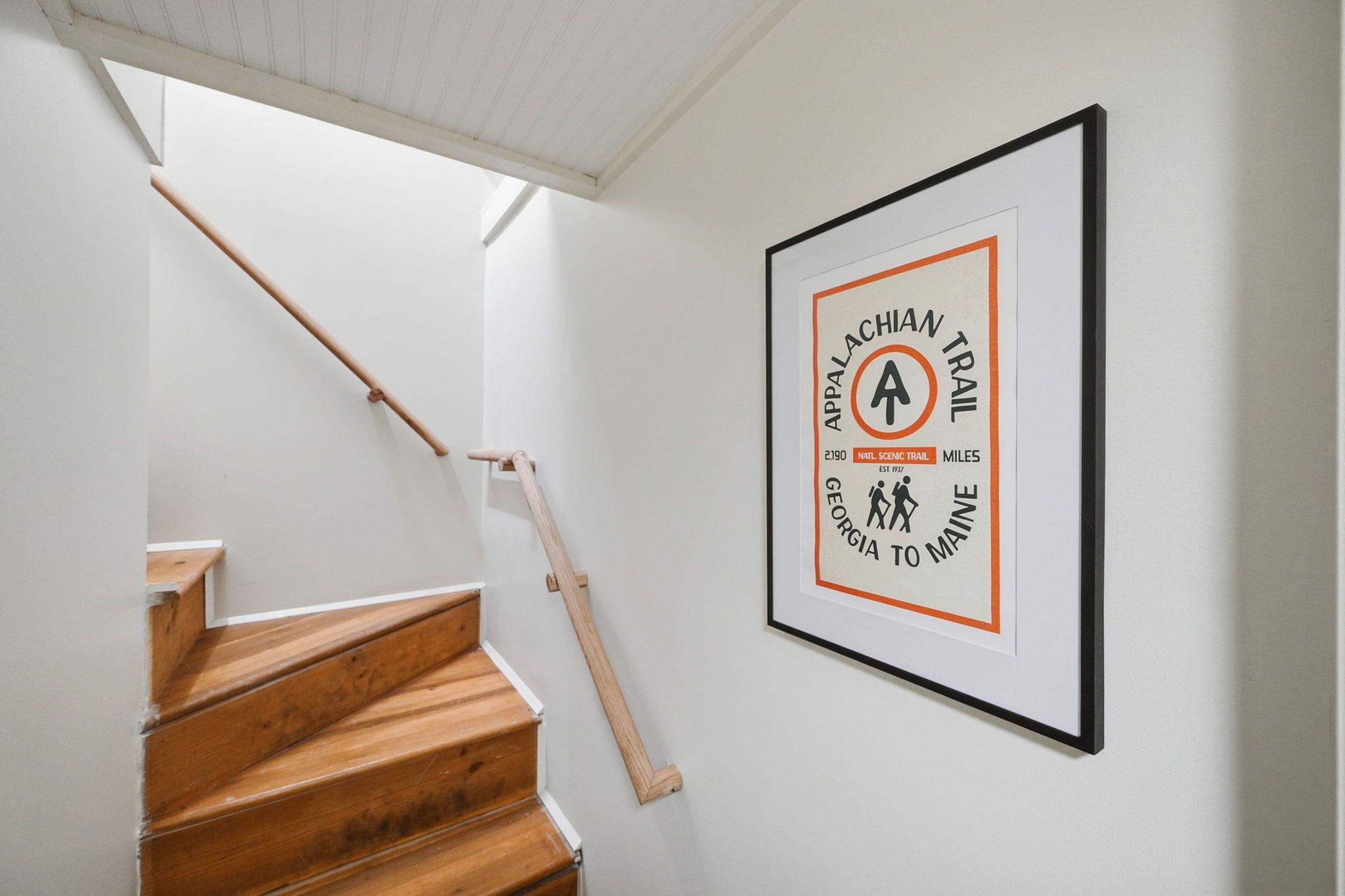 A staircase with wooden steps and a handrail, leading to a landing with a framed sign on the wall.