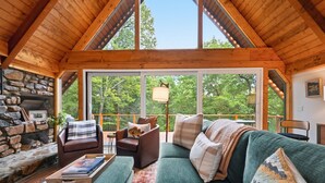 Interior acogedor de una cabaña con chimenea de piedra, un sofá verde y un ventanal con vistas al bosque.