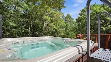 A hot tub on an outdoor deck with a wooden railing, surrounded by trees.