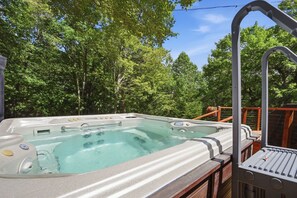 A hot tub on an outdoor deck with a wooden railing, surrounded by trees.