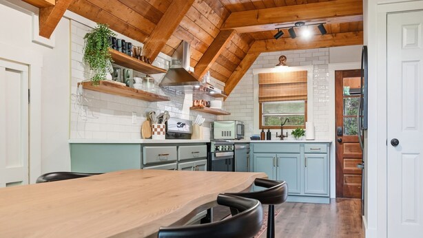 Una cocina con una mesa de madera, taburetes de bar, un microondas y un lavabo.