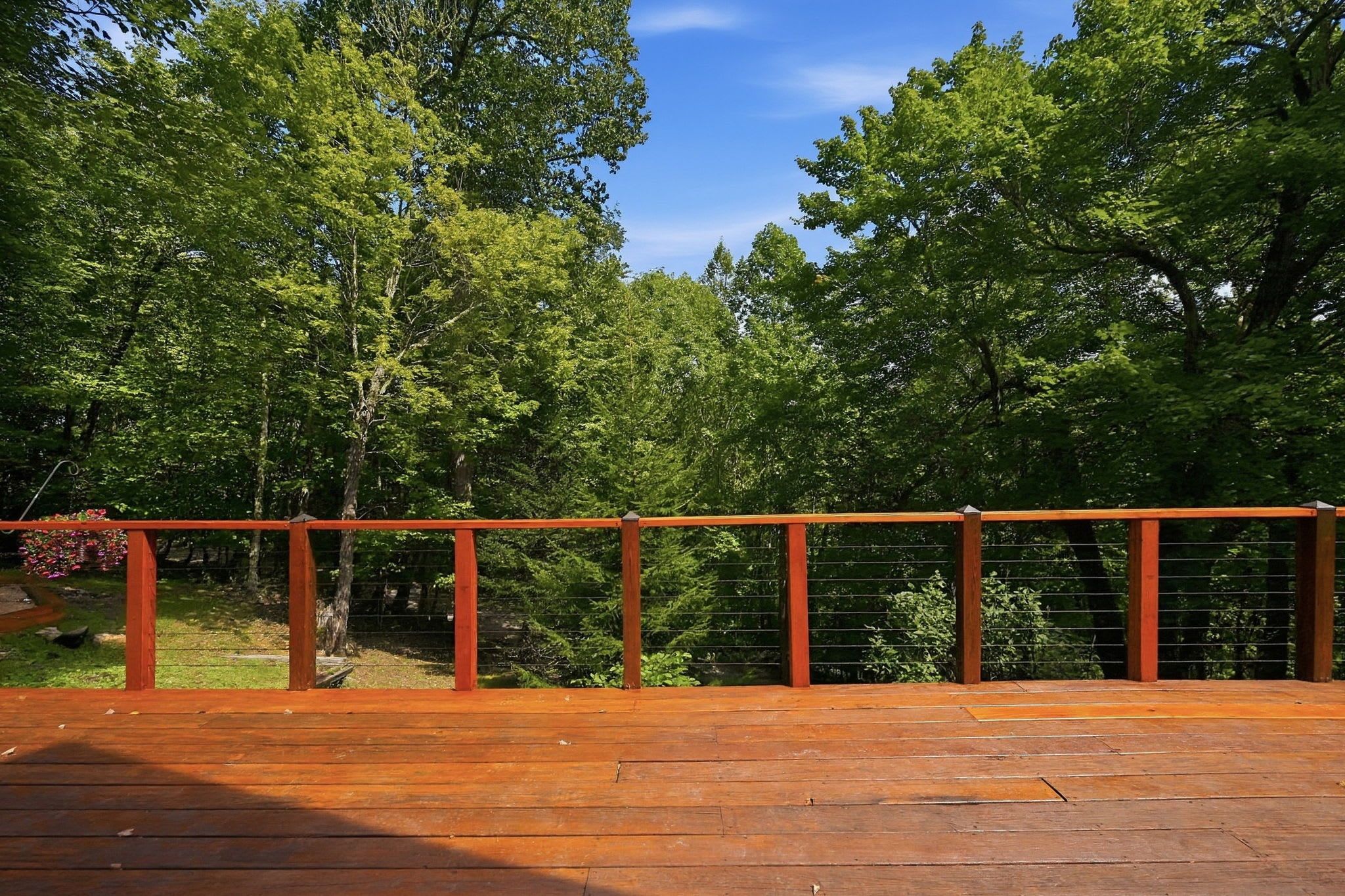 Um deck de madeira com guarda-corpo de metal, cercado por árvores verdes exuberantes.