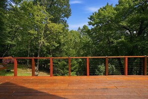 A wooden deck with a metal railing, surrounded by lush green trees.