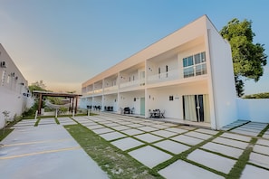 Ein modernes, mehrgeschossiges Gebäude mit flachem Dach, einer überdachten Außenlounge und einem gepflasterten Innenhof mit einem gemusterten Design.