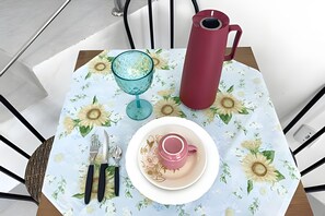 A table with a floral tablecloth, a pink mug, a glass, a knife, and a red thermos. - Apartamento 6 com 2 suítes 450m da praia (Santa Cruz Cabrália)