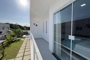A modern balcony with a glass door, a small pool, and a view of a residential area. - Apartamento 6 com 2 suítes 450m da praia (Santa Cruz Cabrália)