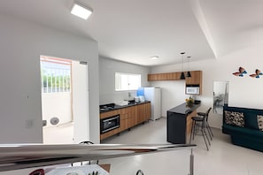 A modern kitchen with wooden cabinets, a black countertop, and a built-in microwave. - Apartamento 6 com 2 suítes 450m da praia (Santa Cruz Cabrália)