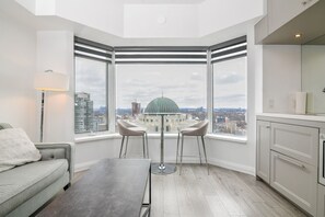 A modern kitchen with a view of the city, a dining area with two chairs, and a sofa. - Modern 1BR with Breathtaking Yorkville View (Toronto)