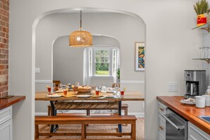 A dining area with a wooden table set for a meal, a hanging light fixture, and a kitchen area with appliances. - Historic 4BR Cottage | Near Downtown and Beach (St. Augustine)