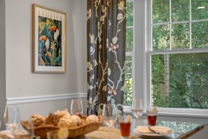 A dining area with a table set for a meal, a framed artwork on the wall, and a window with a view of greenery. - Historic 4BR Cottage | Near Downtown and Beach (St. Augustine)