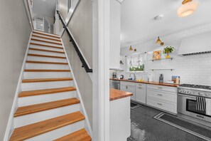 A modern kitchen with white cabinetry, a stainless steel stove, and a black and white patterned rug. - Historic 4BR Cottage | Near Downtown and Beach (St. Augustine)