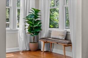 Ein Zimmer mit einer hölzernen Bank, einem Blumentopf und einem Fenster mit weißen Vorhängen.