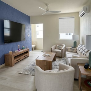Ein Wohnzimmer mit einem Flachbildfernseher, einem Deckenventilator und einem großen Fenster.