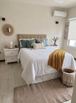 Ein Schlafzimmer mit einem Bett, Nachttischen, einer Wand-Klimaanlage und einem Fenster mit Jalousien.