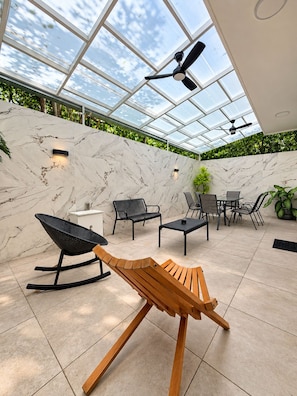 A modern outdoor patio with a glass ceiling, marble walls, and a variety of seating options including a wooden bench, chairs, and a table. - Luxury family villa with a private pool, spacious rooms, and top-notch amenities (Puerto Morelos)